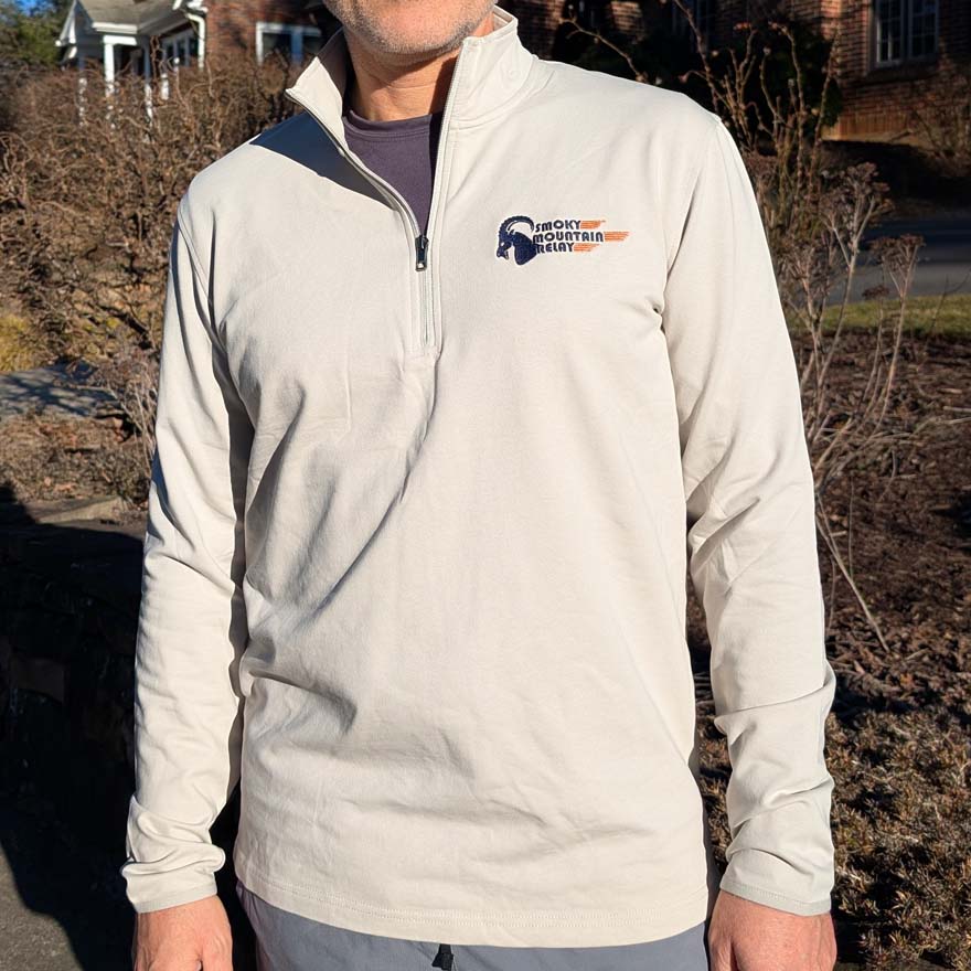 Person wearing a light gray pullover with a Smoky Mountain Relay speed ram logo on the chest outdoors.