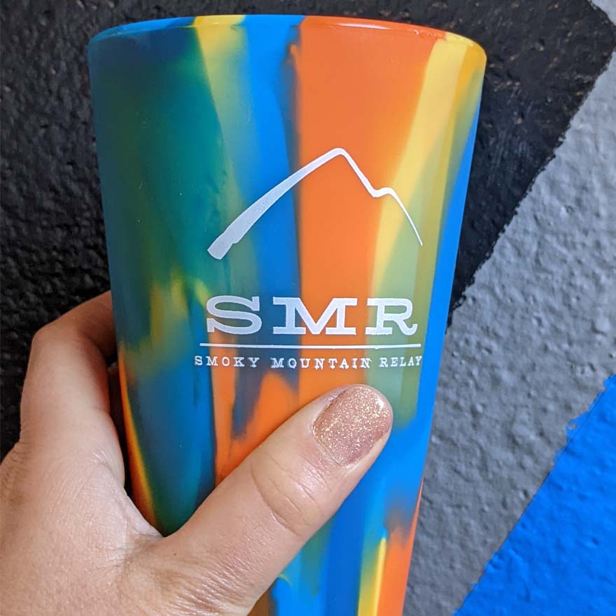 Colorful silicone pint glass with 'SMR Smoky Mountain Relay' logo held by a hand.