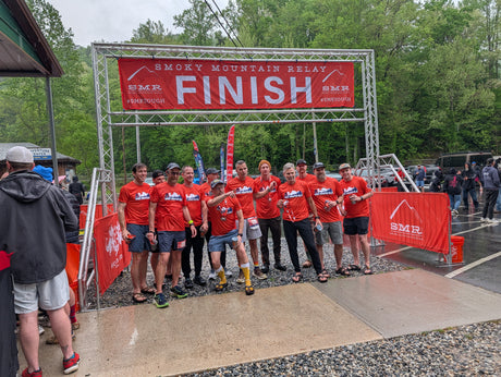 Group of runners in orange official race shirts posing at the finish line of the Smoky Mountain Relay race.
