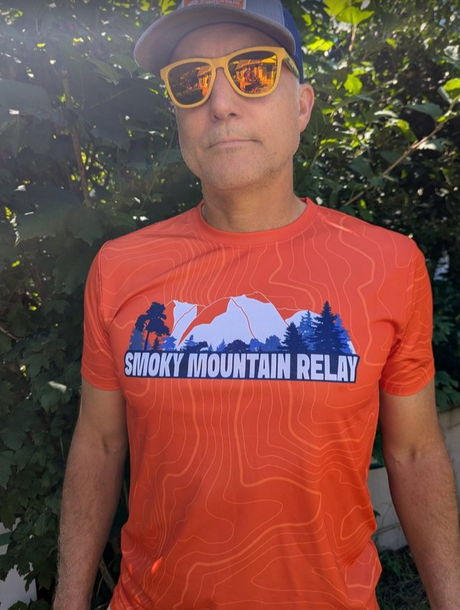 Person wearing an orange 'Smoky Mountain Relay' t-shirt with sunglasses and a cap outdoors.