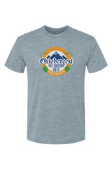 light blue t-shirt with Oktoberfest Half Marathon & 5k logo with blue mountains, green hops in a gold ring on a white background