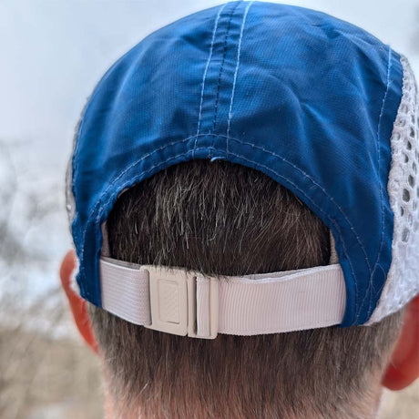 Blue cap with a white mesh back worn by a person, with a blurred background.