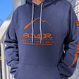 Person wearing a blue hoodie with orange SMR logo text and graphics, standing outdoors.