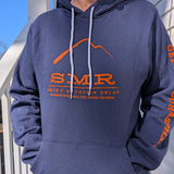 Person wearing a blue hoodie with orange SMR logo text and graphics, standing outdoors.