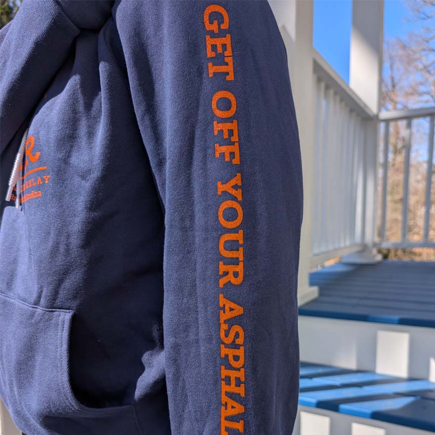 Blue hoodie with orange text 'GET OFF YOUR ASPHALT' on a person outdoors.