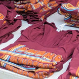 Maroon t-shirts with colorful 'Smoky Mountain Relay' text design folded with colorful graphics on a white surface.