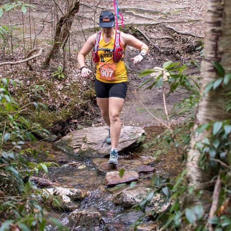 Woman running through a forest with a stream on a trail